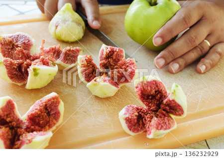 Close-up shot of peeled figs cut up into quarters, showing the red seeds inside, a person's hand on a chopping board with a knife Close-up shot of peeled figs cut up into quarters, showing the red seeds inside, a person's hand on a chopping board with a knife 136232929