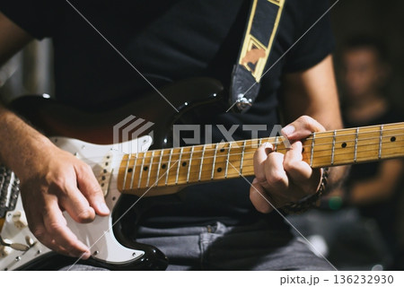 Close-up of a man's hands playing a chord on a sleek shaped electric guitar with a maple neck - live music band performance on stage 136232930