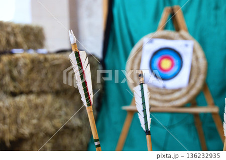 A quiver of traditional medieval arrows against a blurry background of an archery target, in a shooting tournament or competition 136232935