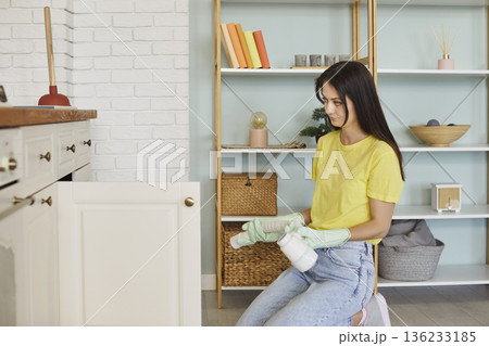 Woman housewife sitting near open kitchen cabinet, domestic care, holding cleaning supplies, spray 136233185