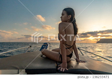 Woman boat sunset, young woman sitting on boat enjoying serene ocean sunset view during summer vacation 136233471