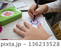 Close-up shot of the hands of a white Caucasian girl drawing a colorful spirograph design on paper 136233528