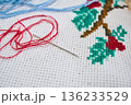 Close-up shot of a hand-made cross stitch design, with colored cotton thread and needle on aida cloth fabric background, with copy space 136233529