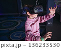 A young white Caucasian girl wearing a VR virtual reality headset playing an immersive video game at an entertainment arcade 136233530