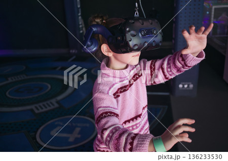 A young white Caucasian girl wearing a VR virtual reality headset playing an immersive video game at an entertainment arcade A young white Caucasian girl wearing a VR virtual reality headset playing an immersive video game at an entertainment arcade 136233530