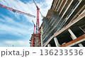 A ground-level worm's view of a construction site, looking up at scaffolding and cranes at the front of a building under construction 136233536