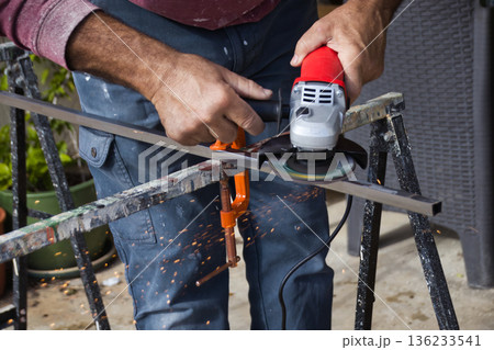 Close-up of the hands of a white Caucasian male holding an angle grinder to smooth the surface of a steel metal rod - home improvement do it yourself concept shot Close-up of the hands of a white Caucasian male holding an angle grinder to smooth the surface of a steel metal rod - home improvement do it yourself concept shot 136233541