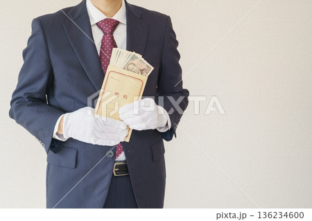 給料袋を持つスーツを着た男性｜一万円札の入った給料袋 136234600
