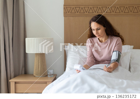 Caucasian middle aged woman measuring blood pressure at home using digital monitor 136235172