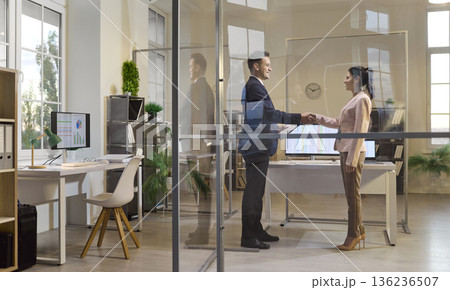 Business partners handshake in glass walled office during formal meeting Business partners handshake in glass walled office during formal meeting 136236507