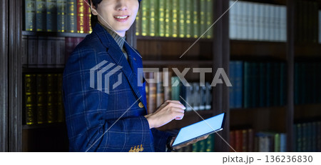 書斎でタブレットを持ち笑顔を見せるスーツ姿の若い日本人男性 136236830