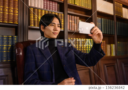 書斎でジャケットを着た若い男性がスマートフ 書斎でジャケットを着た若い男性がスマートフ 136236842