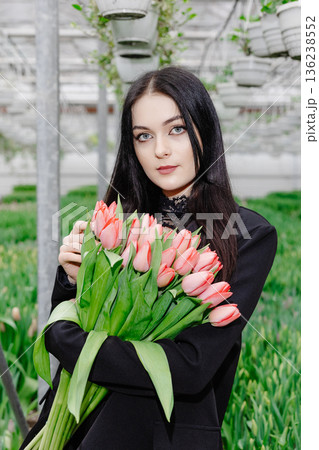 Young woman standing in large greenhouse and holding a blooming tulips in her hands Young woman standing in large greenhouse and holding a blooming tulips in her hands 136238552