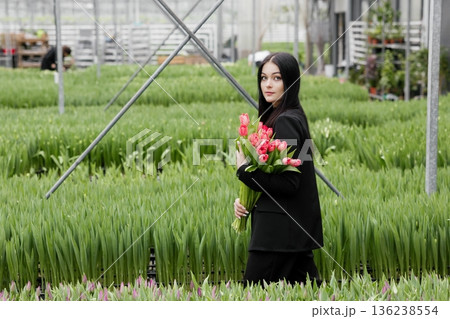 Young woman standing in large greenhouse and holding a blooming tulips in her hands Young woman standing in large greenhouse and holding a blooming tulips in her hands 136238554