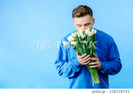 Man holding bouquet of tulips, looking at camera isolated on blue background. Celebration concept Man holding bouquet of tulips, looking at camera isolated on blue background. Celebration concept 136238741