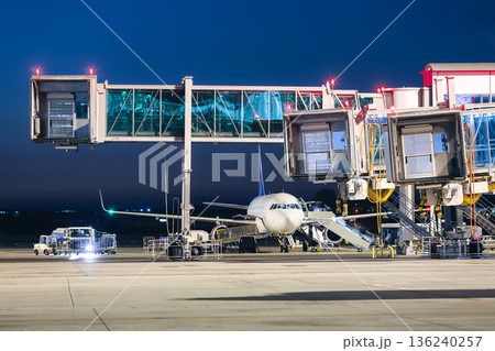 Passenger boarding bridges and airplane at terminal building preparing for departure at night Passenger boarding bridges and airplane at terminal building preparing for departure at night 136240257