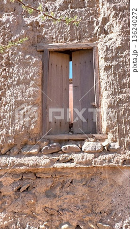 Old Rustic Entrance. Sunlit Cracked Wall Opening. Textured Door With Warm Earthy Hues. Charming Workshop Concealed Behind Aged Door With Textured Surfaces And Inviting Warm Tones 136240272