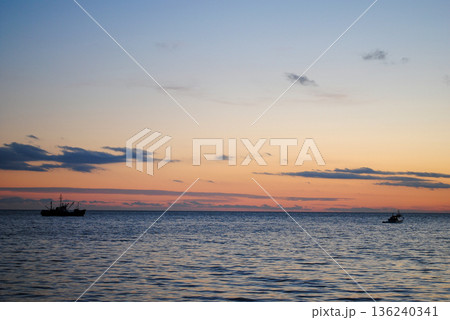 The photograph showcases a stunning view of a sea bay on the Kuril Islands at sunset, with vessels gently resting on the water. 136240341