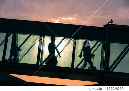 Passengers walking through boarding bridge to airplane at airport Passengers walking through boarding bridge to airplane at airport 136240404