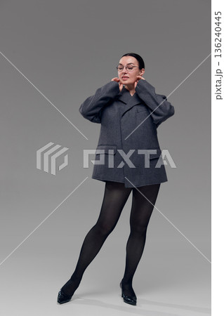Stylish mature woman posing in oversized gray blazer on neutral background. 136240445