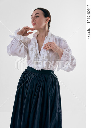 Classic woman in white ruffled blouse posing in studio portrait with soft confidence. 136240449