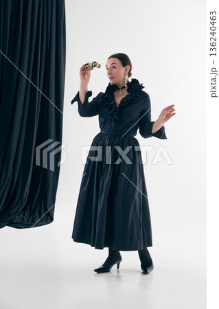 Vintage inspired woman in black ruffled dress holding opera binoculars. Vintage inspired woman in black ruffled dress holding opera binoculars. 136240463