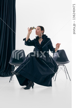 Retro woman using opera glasses in studio with curious elegance 136240471