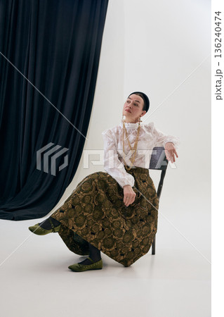Elegant vintage styled woman seated on chair in classic studio setting. Elegant vintage styled woman seated on chair in classic studio setting. 136240474