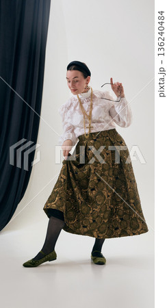 Mature woman in lace blouse and patterned skirt lifting hem with playful focus. Mature woman in lace blouse and patterned skirt lifting hem with playful focus. 136240484