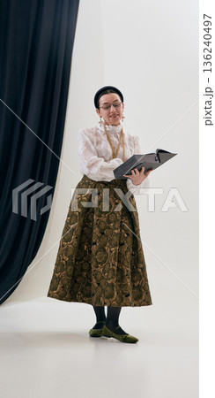 Vintage woman reading book wearing lace blouse and brocade skirt in studio with gentle focus. 136240497