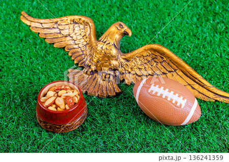An eagle statue is placed bowl of mixed nuts American football on green grass for super bowl sports gathering. 136241359