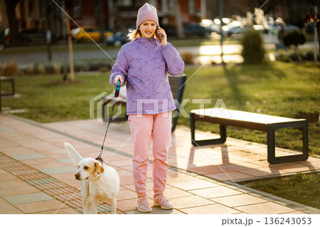 Woman walking dog talking on cell phone in park 136243053