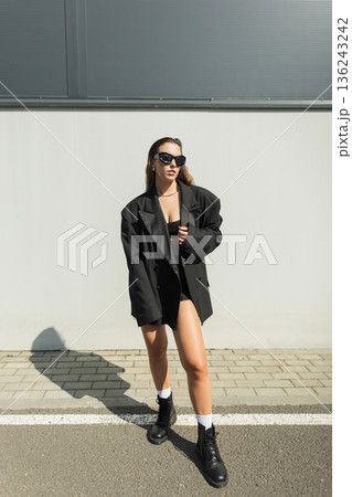 Stylish young woman in black oversized blazer and sunglasses walking confidently in urban street fashion look. Fashion pretty urban lady with sunglasses Stylish young woman in black oversized blazer and sunglasses walking confidently in urban street fashion look. Fashion pretty urban lady with sunglasses 136243242