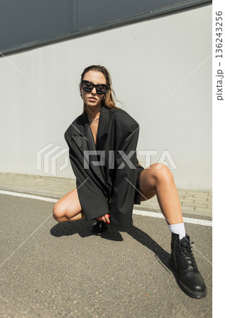 Beautiful glamorous fashion model girl in black clothes with oversized jacket, sunglasses and boots posing on the street near the building. Cool urban lady in sunlight Beautiful glamorous fashion model girl in black clothes with oversized jacket, sunglasses and boots posing on the street near the building. Cool urban lady in sunlight 136243256