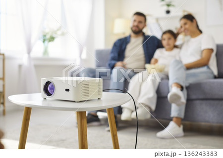 Home projector on table as family watching movie together in living room 136243383