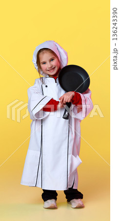 Smiling little girl dressed as chef holding frying pan Smiling little girl dressed as chef holding frying pan 136243390