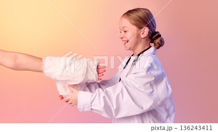 Girl doctor bandaging injured arm during role play. Girl doctor bandaging injured arm during role play. 136243411