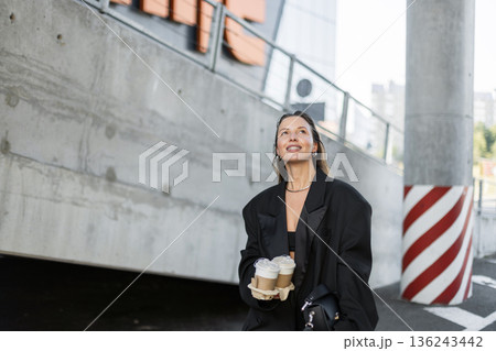 Fashionable girl in oversized blazer and crop top walking outside, holding takeaway coffee and radiating happiness. 136243442