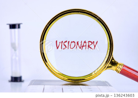 A golden magnifying glass centers on the red word visionary, placed on a white background. An hourglass and calculator indicate time and strategic thought 136243603