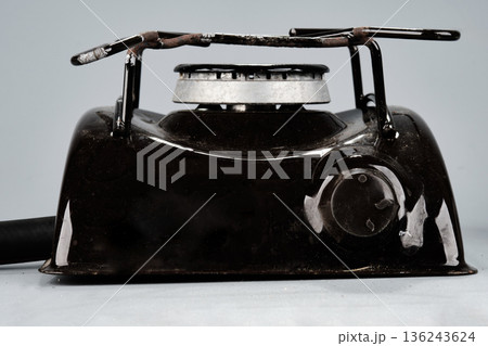 Black portable cooking appliance stands on a neutral grey surface. It displays a silver burner, a pot stand, and a control knob, used for heating food 136243624