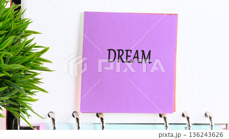 A bright purple sticky note clearly shows the word DREAM written in black, affixed to a white binder A bright purple sticky note clearly shows the word DREAM written in black, affixed to a white binder 136243626