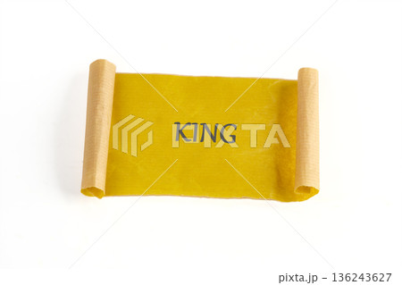 Bright yellow scroll unrolled on a white surface shows the word KING. Rolled edges of brown paper are visible on each side 136243627