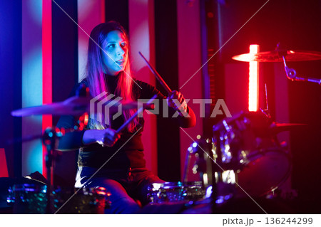 Female drummer performing on stage with colorful lighting 136244299