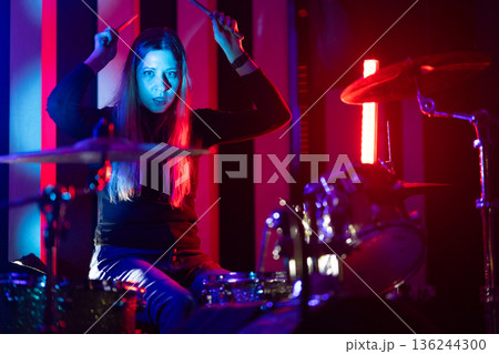 Energetic female drummer performing live music under vibrant stage lights Energetic female drummer performing live music under vibrant stage lights 136244300