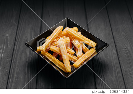 Sugar dusted churros sticks in black bowl on dark wooden background with copy space Sugar dusted churros sticks in black bowl on dark wooden background with copy space 136244324