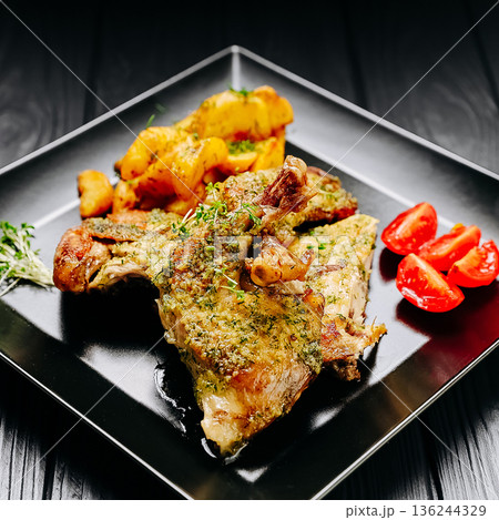 Herb roasted chicken legs with baked potatoes and cherry tomatoes on black plate, dark table Herb roasted chicken legs with baked potatoes and cherry tomatoes on black plate, dark table 136244329