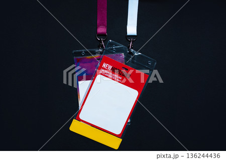 Empty name tag with colorful design hanging on a white lanyard against a dark background. Perfect for illustrating events, conferences, or identification concepts. Free copy space for design 136244436