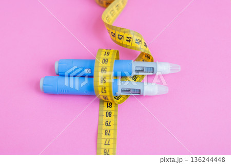Close-up of insulin pens tied with measuring tape on pink background, symbolizing control of diabetes and healthy body weight. drugs injection ozempic for weight loss 136244448