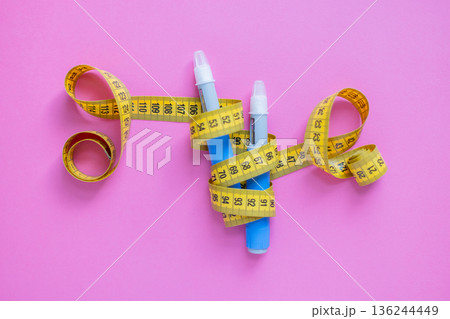 Insulin injection pens and measuring tape on pink surface. Concept of obesity control, diabetes care, and modern medication. drugs injection ozempic for weight loss 136244449