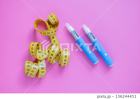 Two blue insulin pens and a yellow measuring tape on a pink background, symbolizing weight loss, diabetes treatment, and medical control. drugs injection ozempic for weight loss Two blue insulin pens and a yellow measuring tape on a pink background, symbolizing weight loss, diabetes treatment, and medical control. drugs injection ozempic for weight loss 136244451